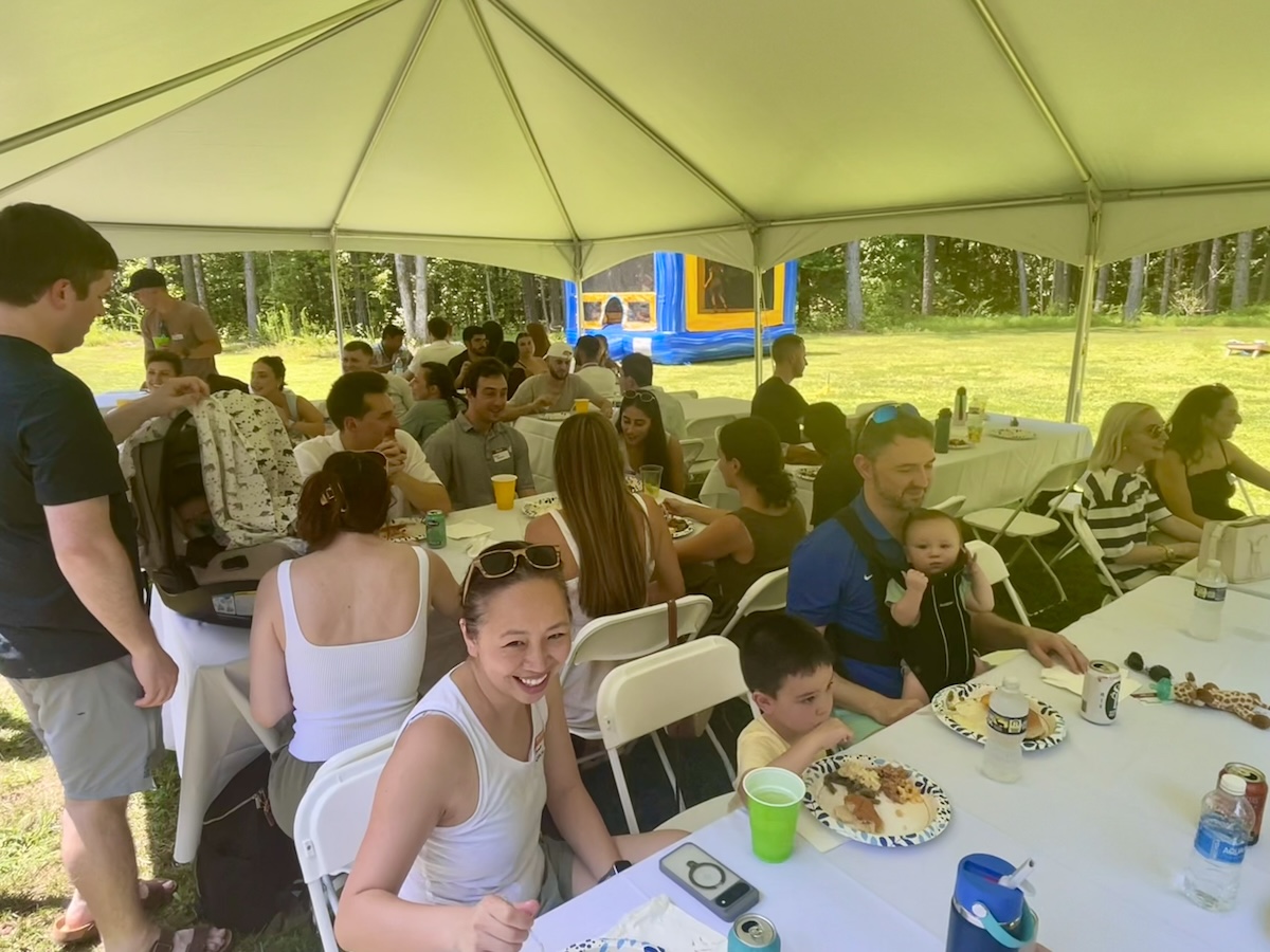 People outside seated and standing, under a tent