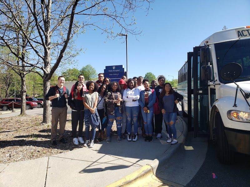 Group of high school students standing next to a bus